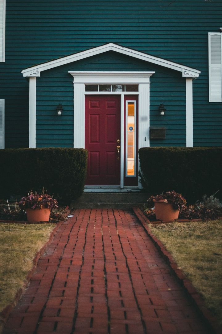 A red front door with a glass sidelight on a dark green house